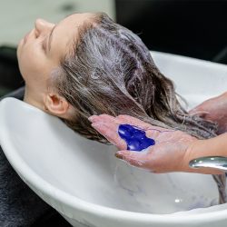 Purple shampoo being applied to blonde hair at the salon backwash