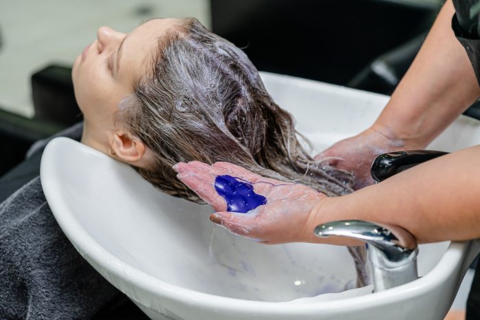 Purple shampoo being applied to blonde hair at a salon backwash
