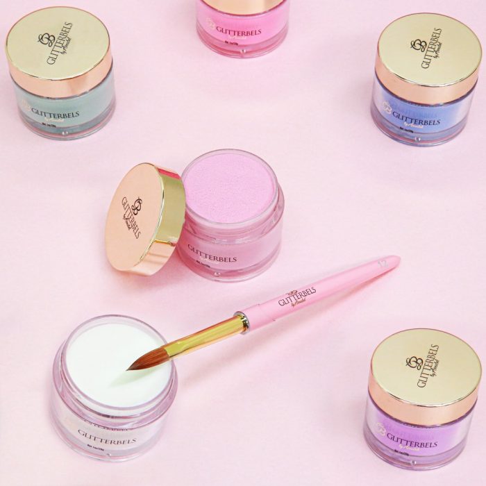 A selection of Glitterbels acrylic powder pots with an acrylic nail brush on a light pink background