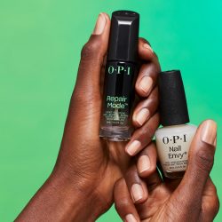 OPI Repair Mode nail serum and OPI Nail Envy nail strengthener in hands on a green background