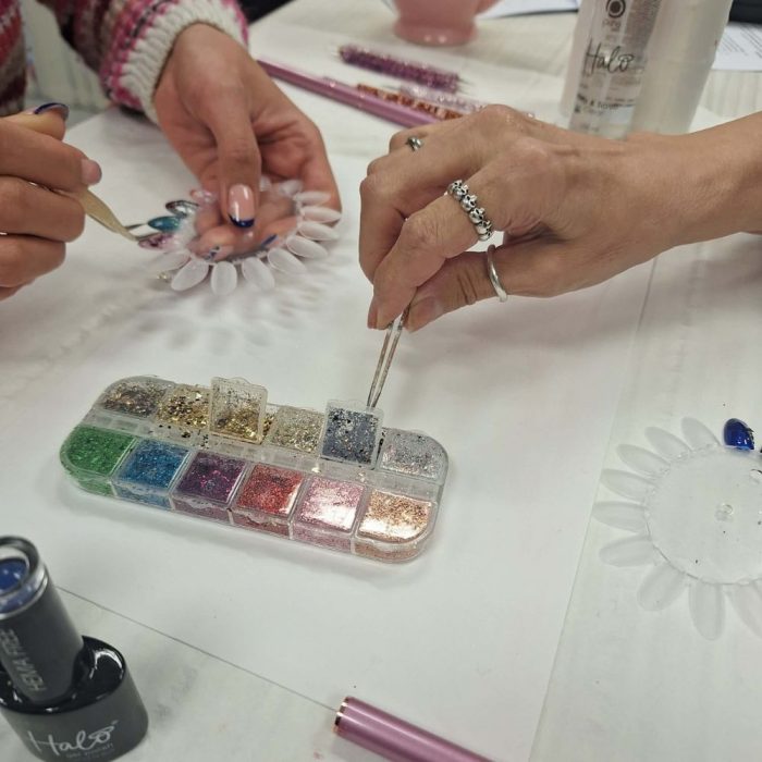 image shows students using nail glitter on nail art course