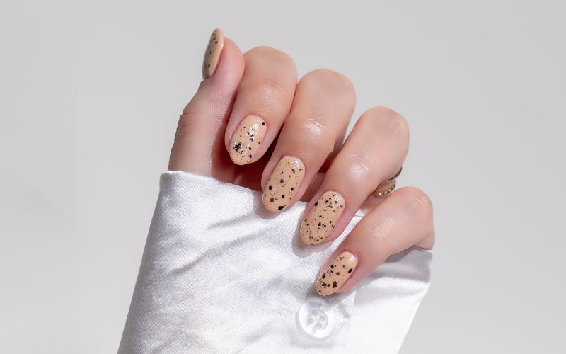 image shows beige and black speckled nails